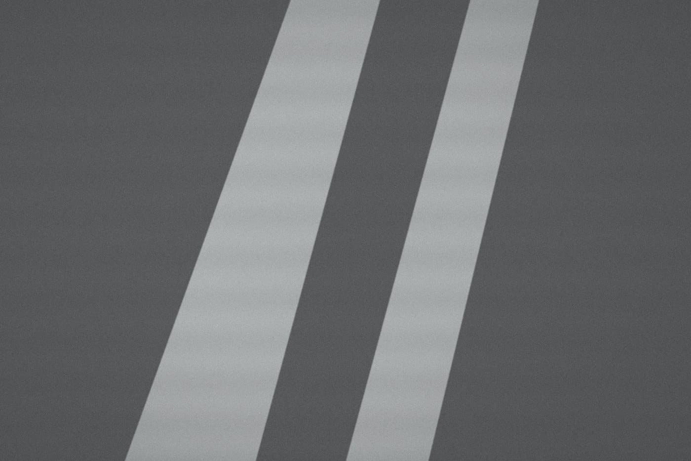 Two pale diagonal stripes on a grey road, before editing