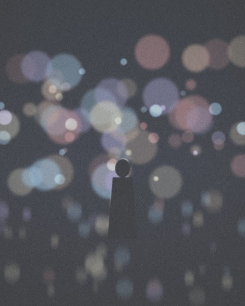 A lone silhouette against soft, muted lights at night, before editing